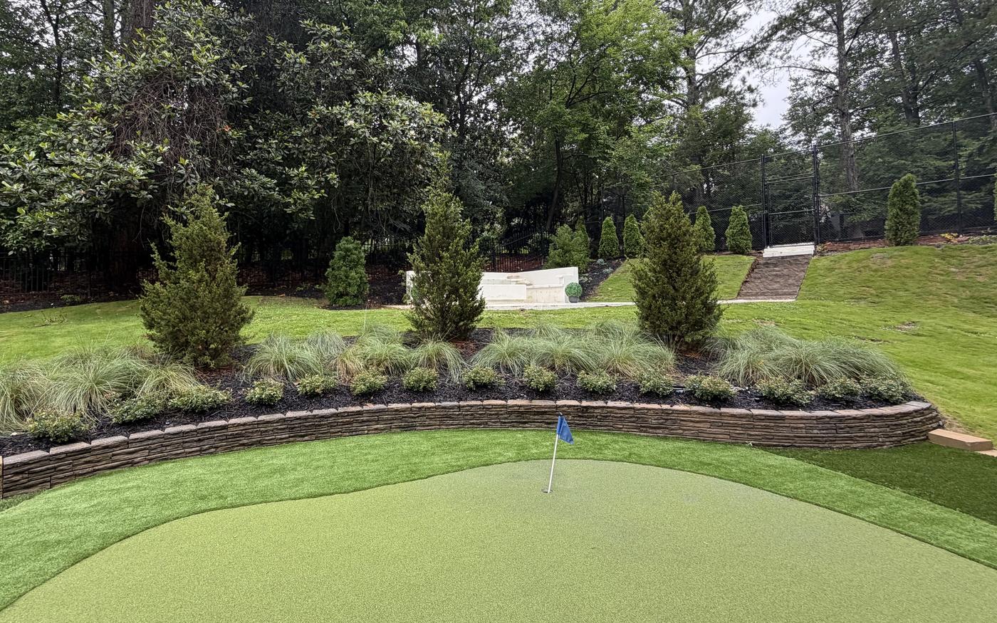 Backyard putting green framed by stone wall and evergreens